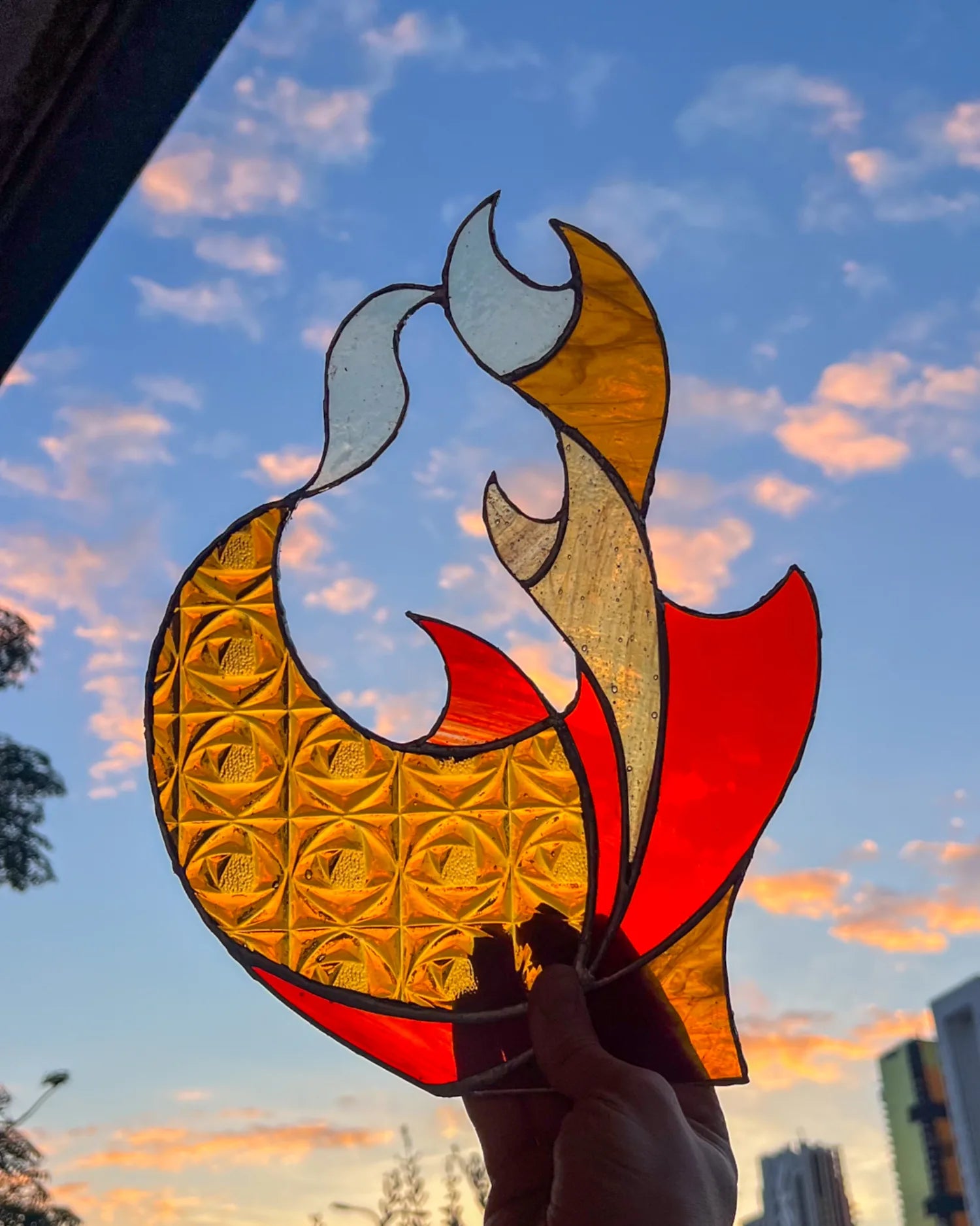 A small amber and red stained-glass flame study held against an evening sky