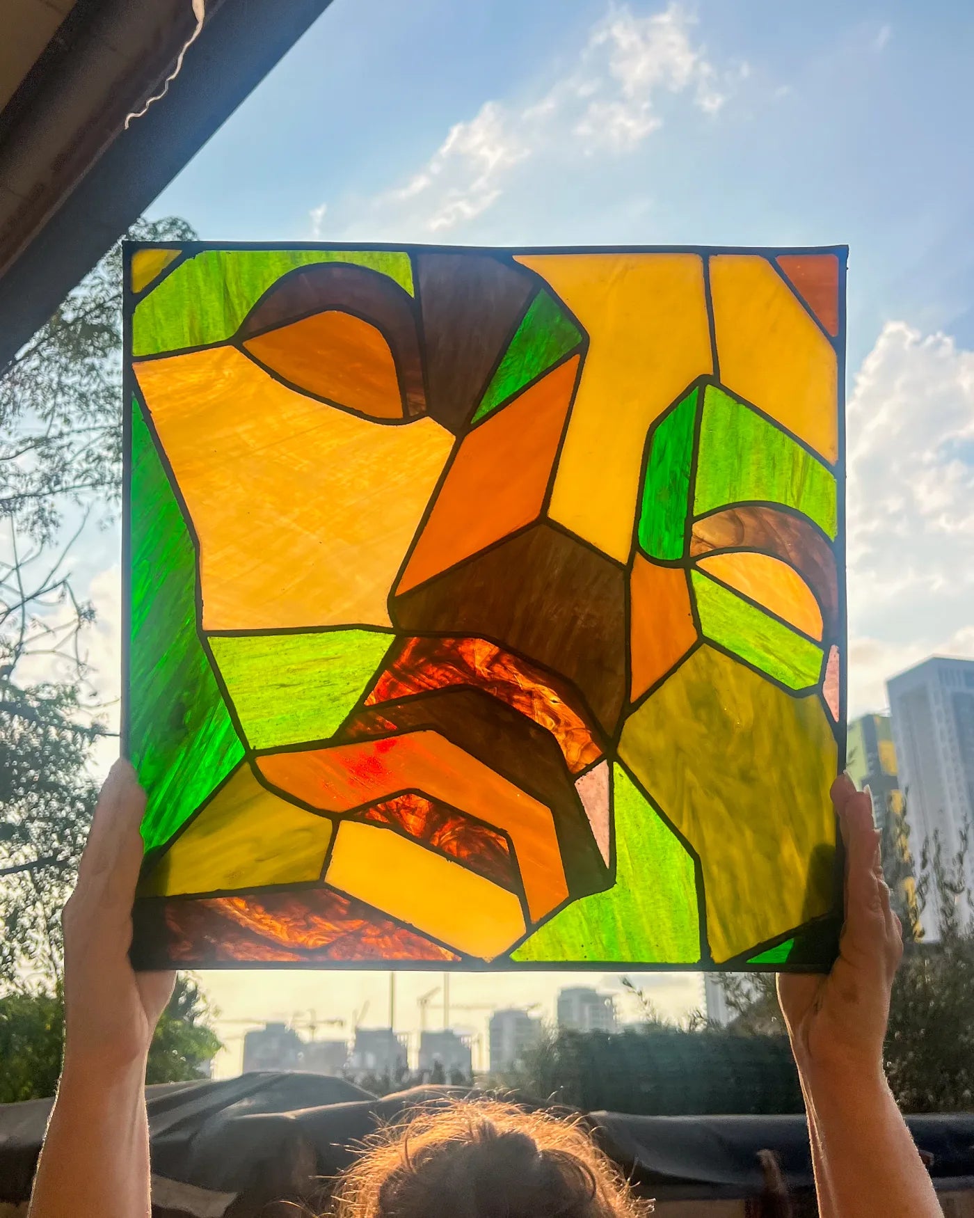 Amber and green geometric stained-glass portrait held to daylight